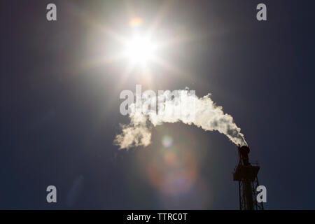Basso angolo di visualizzazione ad emissione di fumo dalla ciminiera alla raffineria di petrolio durante la giornata di sole Foto Stock