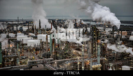 Angolo di Alta Vista della raffineria di petrolio contro il cielo nuvoloso durante il tramonto Foto Stock