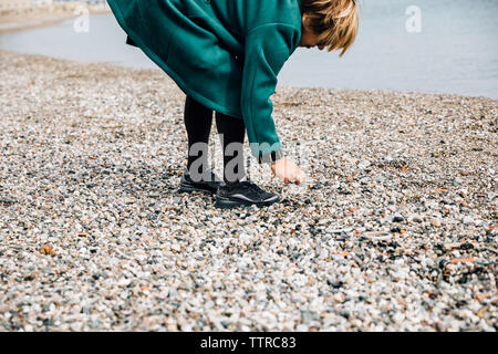 Vista laterale di un senior donna raccolta di rocce in riva al mare Foto Stock