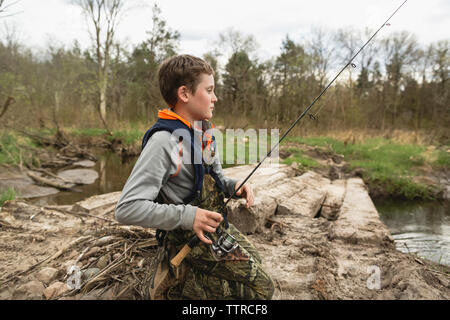 Vista laterale del ragazzo di pesca sul lungolago in foresta Foto Stock