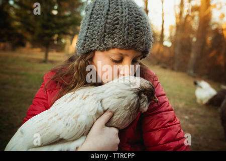 Ragazza baciare il pollo mentre si sta in piedi in azienda agricola di pollame Foto Stock