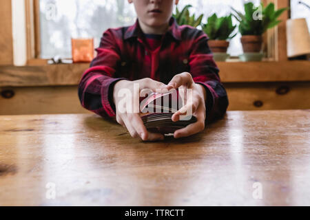Sezione mediana del ragazzo adolescente rimescolare le carte sul tavolo di legno a cottage Foto Stock