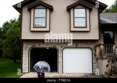 Angolo di Alta Vista del ragazzo tenendo un ombrello mentre in piedi contro la casa Foto Stock