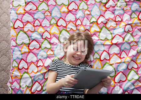 Vista aerea del sorridente ragazza con tavoletta digitale e giacente sul letto Foto Stock