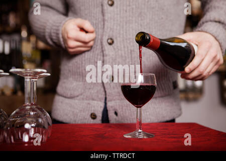 Sezione mediana dei maschi di Sommelier versando il vino rosso in vetro al negozio Foto Stock