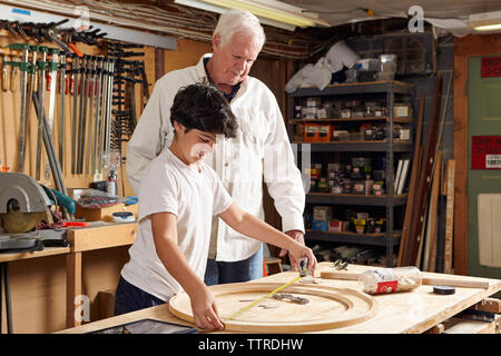 Carpenter guardando il ragazzo di misurazione anello di legno in officina Foto Stock