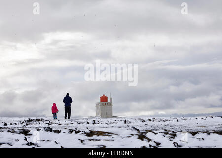 Vista posteriore del padre e figlia in piedi su paesaggi innevati contro il faro e il cielo nuvoloso Foto Stock