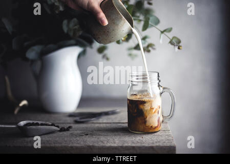 Immagine ritagliata della donna versando il latte nel caffè Foto Stock