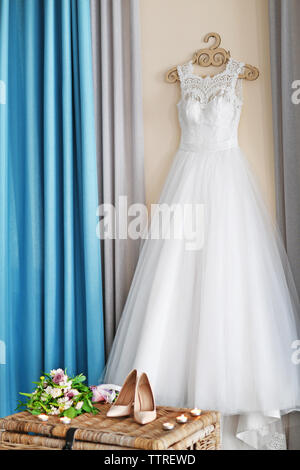 Scarpe sul petto di vimini e abito da sposa appeso alla parete in camera Foto Stock