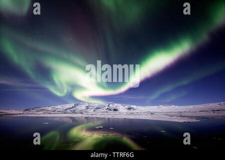 Una vista maestosa dell'aurora boreale oltre il lago ghiacciato al tramonto Foto Stock