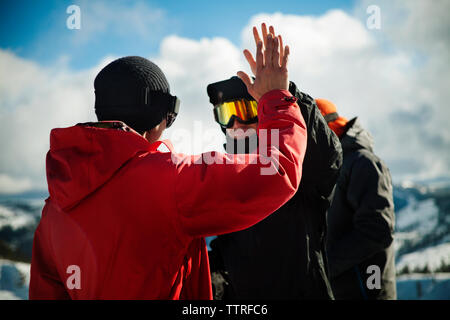 Amici in un abbigliamento caldo alta fiving contro sky Foto Stock