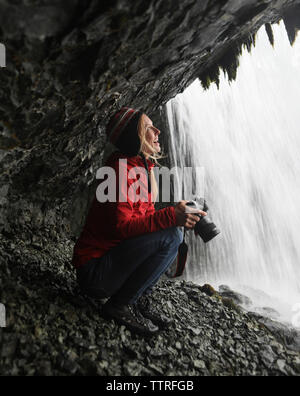 Femmina allegro escursionista guardando a cascata mentre tenere la fotocamera Foto Stock