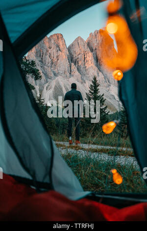 Vista posteriore di uomo in piedi contro montagne visto attraverso la tenda Foto Stock