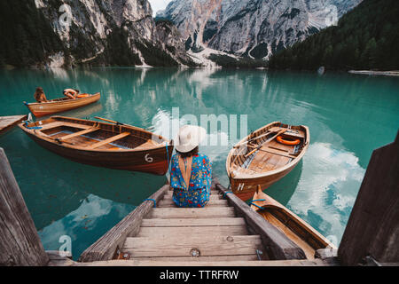 Vista posteriore della donna seduta sui gradini in legno nel Lago di Braies contro le montagne Foto Stock