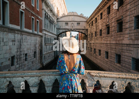 Vista posteriore della donna che indossa hat permanente, mentre dalla ringhiera sul ponte tra gli edifici Foto Stock