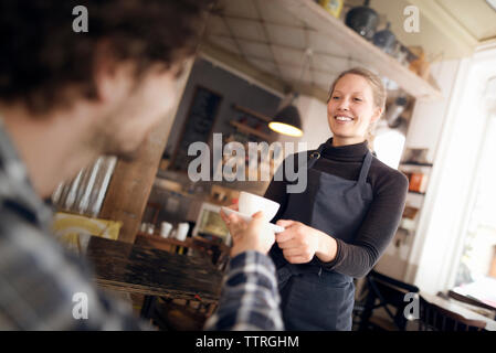 Felice cameriera che serve caffè all uomo in cafe Foto Stock