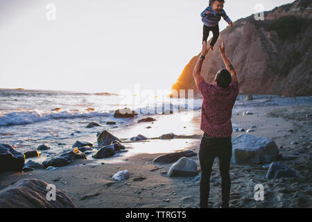 Vista posteriore del giocoso padre figlio di lancio in aria a spiaggia Foto Stock