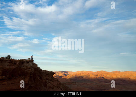 Vista in lontananza silhouette escursionista con il cane in piedi sulla cima della montagna contro il cielo nuvoloso Foto Stock