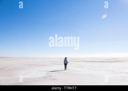 Vista posteriore della donna che cammina al grande lago salato contro il cielo blu durante la giornata di sole Foto Stock