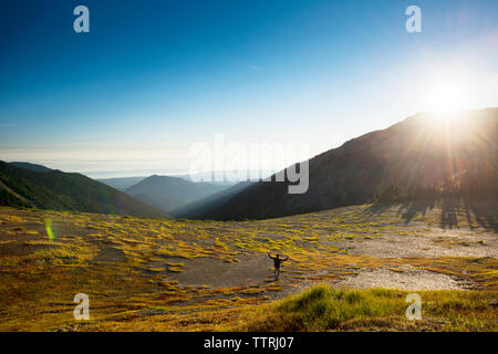 Vista in lontananza ragazzo in piedi sul campo contro la montagna nella giornata di sole Foto Stock