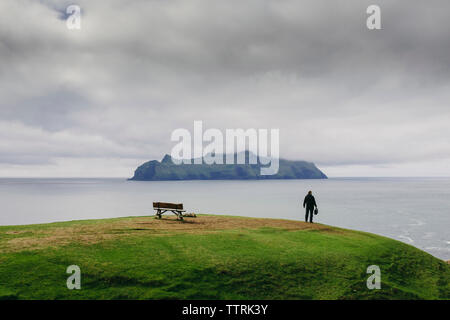 Escursionista guardando a vista mentre in piedi sulla collina dal mare contro nuvole temporalesche Foto Stock