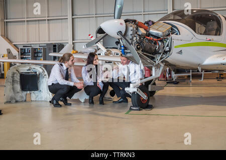 Engineer che mostra la ruota di aereo a tirocinanti mentre accovacciato sul pavimento in hangar Foto Stock