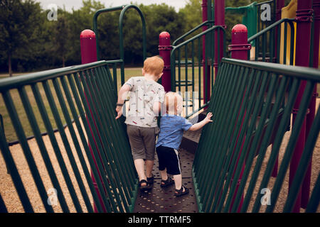 Vista posteriore dei fratelli camminando sulla giungla della palestra presso il parco giochi Foto Stock