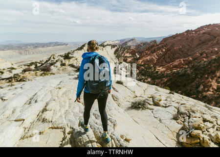 Vista posteriore di un escursionista femmina con zaino camminando su roccia durante la giornata di sole Foto Stock