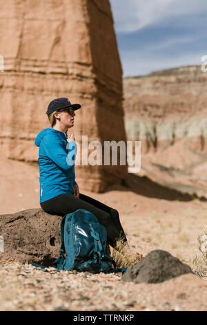 Vista laterale di un escursionista femmina con zaino rilassante mentre è seduto sulla roccia del deserto durante la giornata di sole Foto Stock