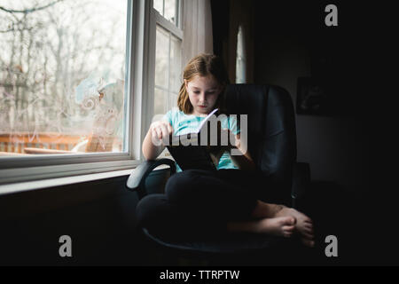 Per tutta la lunghezza della ragazza studiare mentre è seduto su una sedia dalla finestra a casa Foto Stock