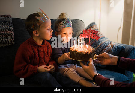 I bambini guardando torta di compleanno detenute da padre a casa Foto Stock