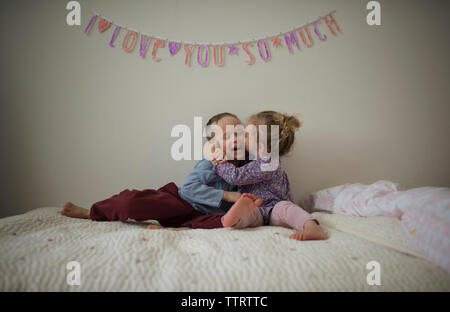 Felice suor kissing fratello mentre è seduto sul letto di casa Foto Stock