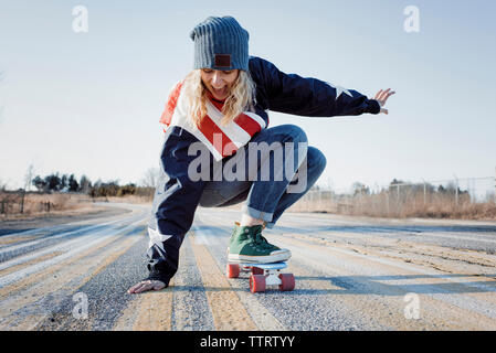 Lunghezza completa di giocosa donna lo skateboard su strada durante il periodo invernale Foto Stock