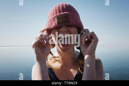 Donna che indossa knit hat urlando contro il mare durante la giornata di sole Foto Stock
