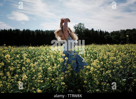 Felice ragazza con braccia alzate in piedi in mezzo a piante contro sky Foto Stock