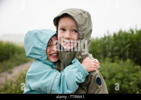 Felice suor abbracciando il fratello mentre in piedi contro piante durante la stagione delle piogge Foto Stock
