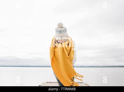 Una donna avvolta in una sciarpa sorridente mantenendo calda in spiaggia Foto Stock