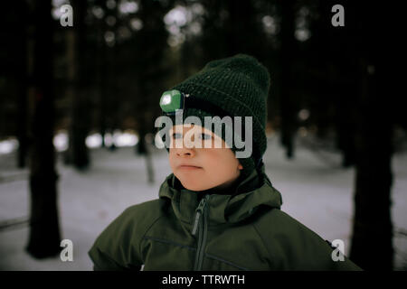 Ragazzo giovane di età compresa tra i 6 piedi al di fuori nella neve con la torcia da testa camping Foto Stock