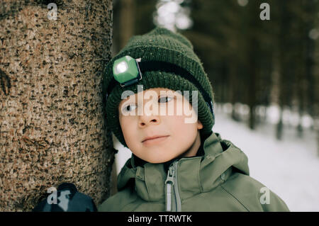Ragazzo giovane appoggiato su di un albero di pensare con la torcia da testa su in inverno Foto Stock