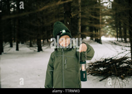 Ragazzo in piedi in una coperta di neve forest holding lanterna torcia e pensare Foto Stock