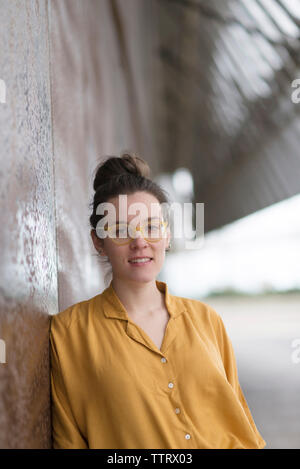 Ritratto di fiducioso imprenditrice indossando occhiali mentre in piedi dalla parete Foto Stock