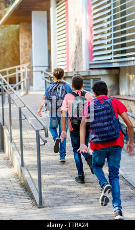 Vista posteriore di amici con zaini in esecuzione sul marciapiede Foto Stock
