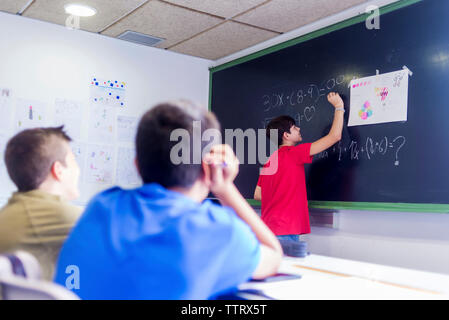 Ragazzo che spiega la matematica a maschio amici in aula Foto Stock