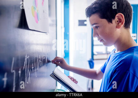 Vista laterale di scolaro praticare la matematica sulla lavagna in aula Foto Stock