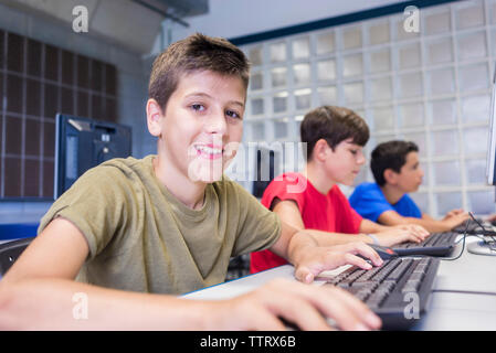 Ritratto di scolaro utilizzando i computer desktop con gli amici in aula Foto Stock