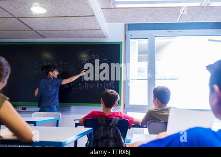 Vista posteriore del maestro femmina spiegando la matematica per gli studenti in aula Foto Stock