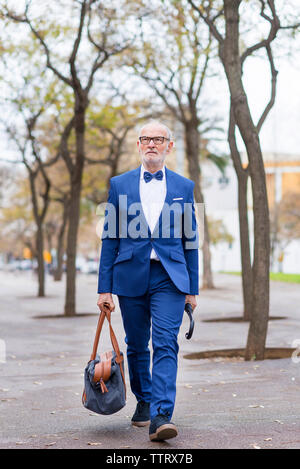Senior uomo indossare tuta portare i bagagli mentre si cammina sul sentiero in città Foto Stock
