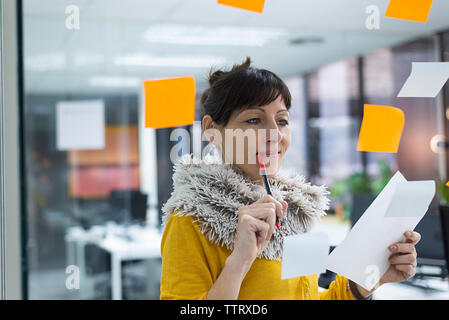 Imprenditrice iscritto sulla finestra in ufficio creativo visto attraverso il vetro Foto Stock