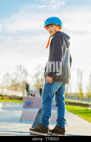 Vista posteriore del giovane pattinatore permanente al skateramp guardando indietro alla fotocamera Foto Stock