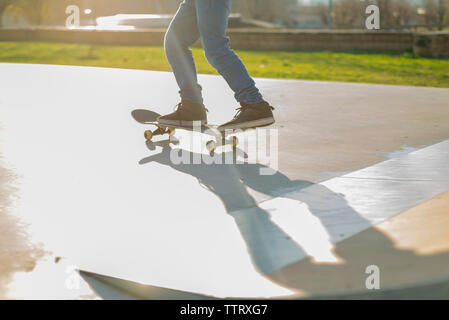 Basso angolo vista del pattinatore gambe a cavallo su skatepark in sunset Foto Stock